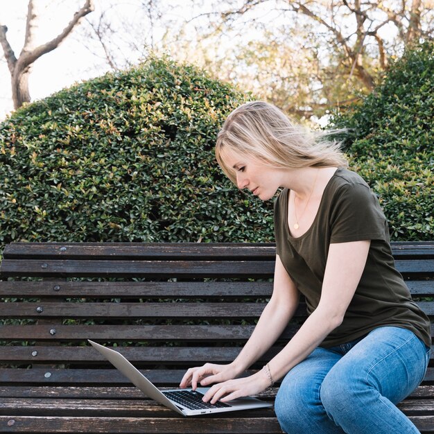 Widok z boku kobieta używa laptop na ławce