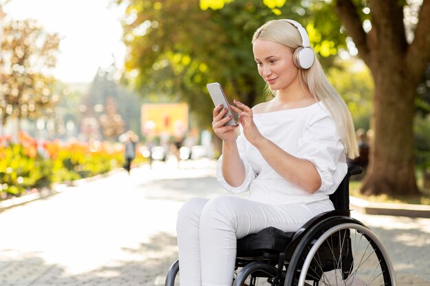 Widok z boku kobiety na wózku inwalidzkim ze smartfonem i słuchawkami