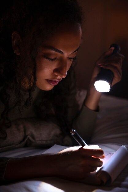 Widok z boku kobiety piszącej w łóżku z latarką