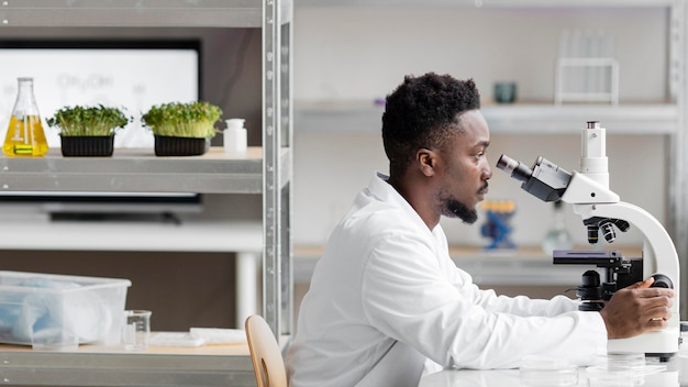 Bezpłatne zdjęcie widok z boku mężczyzny badacza w laboratorium patrząc przez mikroskop