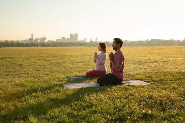 Bezpłatne zdjęcie widok z boku mężczyzny i kobiety medytujących na zewnątrz na matach do jogi