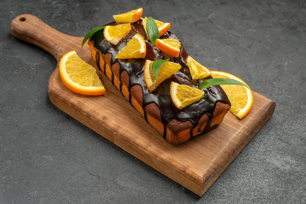 Widok z boku na pyszne ciasta ozdobione pomarańczą i czekoladą na desce do krojenia na czarnym stole