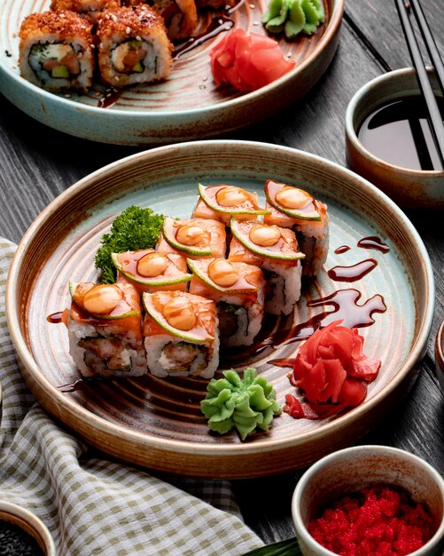 Widok z boku na roladki sushi z krewetkami, awokado i serem śmietankowym podawane z imbirem i wasabi na talerzu na drewnie