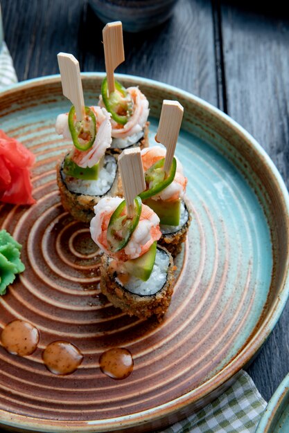 Widok z boku na zestaw pieczonych rolad sushi z krewetkami podawanych z wasabi i imbirem na talerzu na drewnie