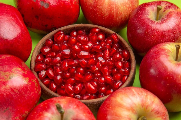 Widok z boku owocuje apetycznymi nasionami granatu w brązowej misce z jabłkami na stole