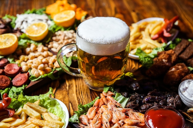 Widok z boku piwo przekąski kiełbaski groch nasiona i frytki z kawałkami cytryny na stojaku ze szklanką piwa