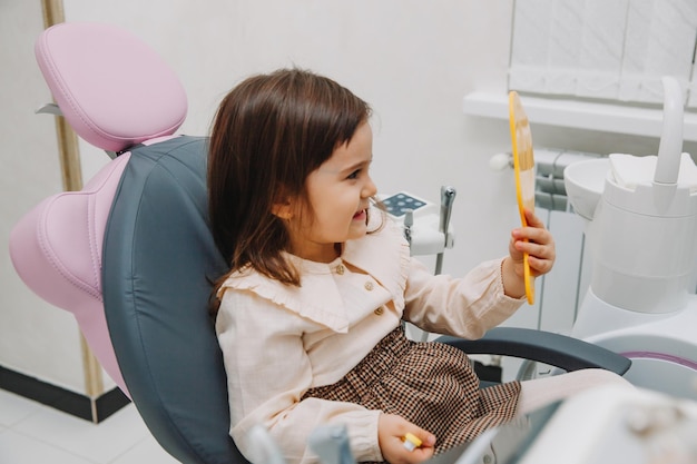 Widok z boku portret dziewczynki patrząc w lustro w stomatologii dziecięcej po operacji stomatologicznej.