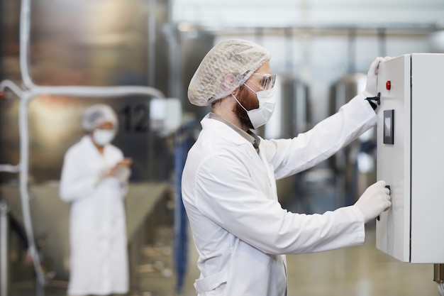 Widok z boku portret męskiego pracownika obsługującego maszyny w zakładzie chemicznym podczas noszenia fartucha i odzieży ochronnej, miejsce kopiowania