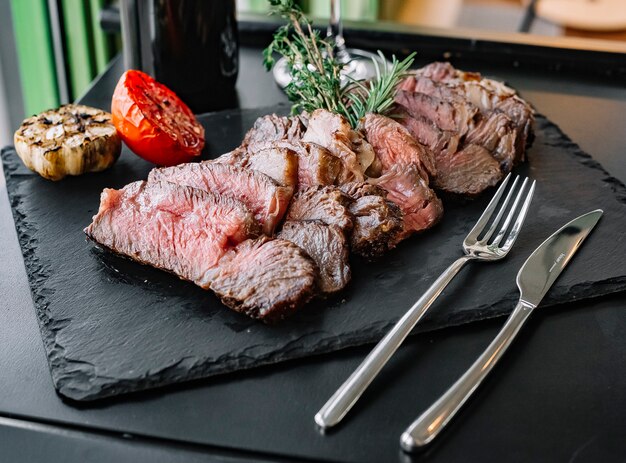 Widok z boku posiekany stek z rozmarynem i grillowanym pomidorem i czosnkiem