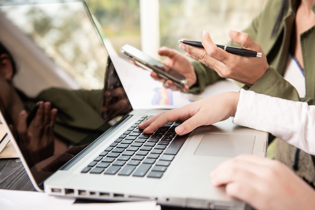 Widok z boku rąk bizneswomanu za pomocą komputera przenośnego umieszczonego na messy pulpicie pakietu office. praca zespołowa z wykresem kosztów analizy ludzi biznesu na biurku w sali konferencyjnej.