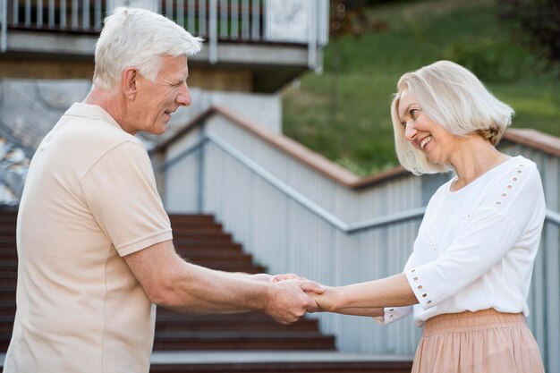 Widok z boku romantycznej i kochającej pary starszych, trzymając się za ręce na zewnątrz