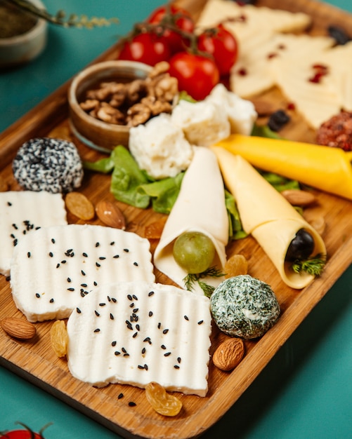 Bezpłatne zdjęcie widok z boku różnych rodzajów sera z winogronami orzechowymi i wiśniowymi ziemniakami na drewnianym talerzu
