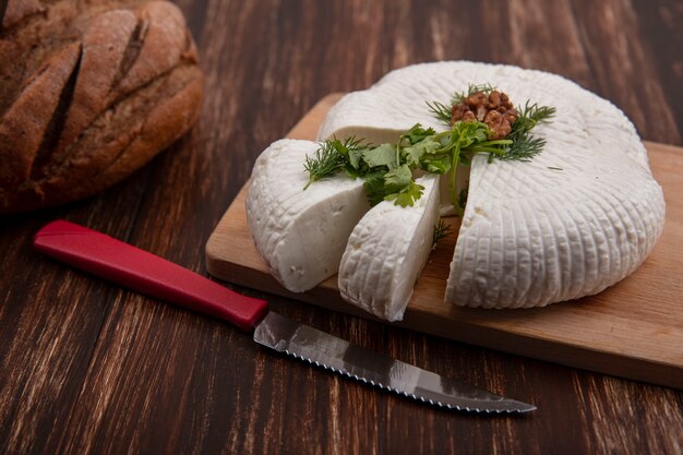 Widok z boku sera feta na stojaku z nożem i bochenkiem chleba na tle drewnianych