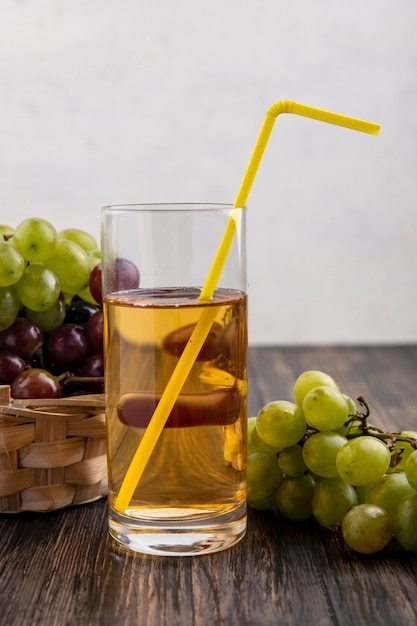 Widok z boku soku winogronowego w szkle i winogron w koszu i na powierzchni drewnianych i białym tle