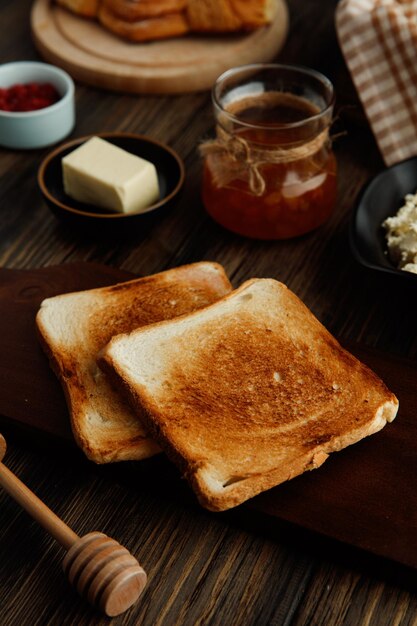 Widok z boku suszonych kromek chleba na desce do krojenia z dżemem masło czerwonych porzeczek na drewnianym tle