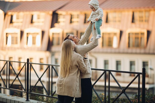 Widok z boku szczęśliwego męża i żony z ich uroczym dzieckiem Przystojny mężczyzna trzymający małe dziecko i piękna kobieta przytulająca go od tyłu Młoda rodzina w zwykłych ubraniach spacerująca razem w słoneczny dzień