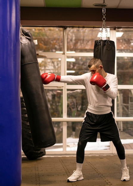 Widok z boku trenującego boksera z workiem treningowym obok ringu