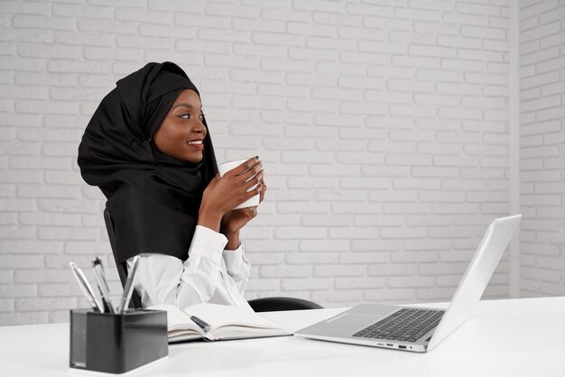 Widok z boku uśmiechniętej kobiety w czarnym hidżabie pijącej kawę