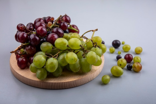 Widok z boku winogron na deska do krojenia z jagodami winogron na szarym tle