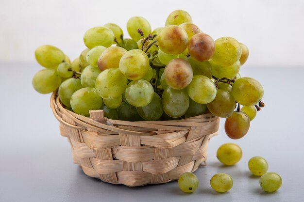 Widok z boku z białych winogron w koszu na szarej powierzchni i białym tle