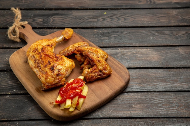 Widok z boku z bliska frytki frytki i apetyczny kurczak miska ketchupu na desce do krojenia na drewnianym stole