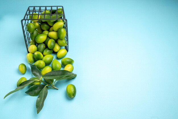 Widok z boku z daleka owoce zielono-żółte owoce z liśćmi w koszu na niebieskim stole