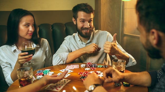 Widok z boku zdjęcie przyjaciół siedzących przy drewnianym stole. przyjaciele bawią się podczas gry w gry planszowe.