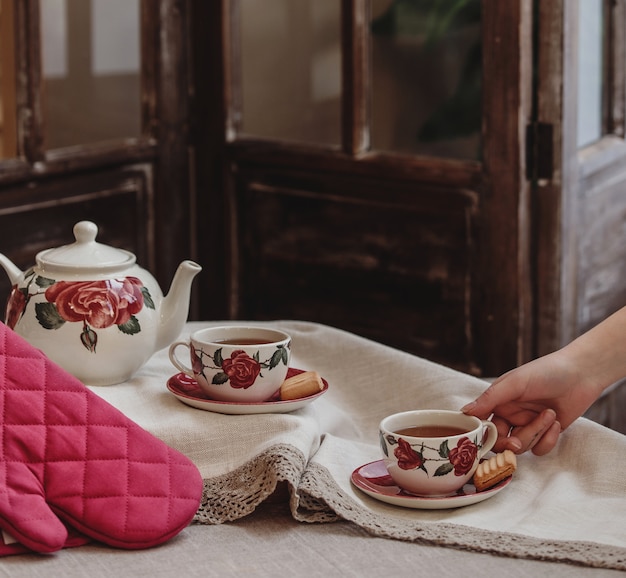Bezpłatne zdjęcie widok z boku zestawu herbaty w kwiatowy wzór róży z czajnikiem i filiżanką z ciasteczkami na obrusie