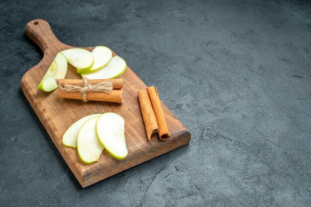 Widok z dołu plasterki jabłka i laski cynamonu na desce do krojenia na ciemnym stole z wolną przestrzenią