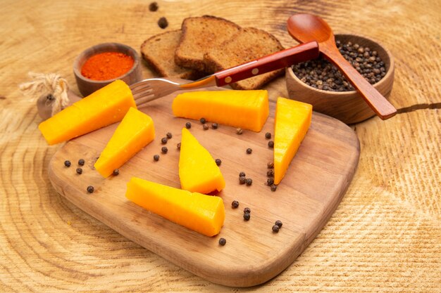 Widok z dołu ser na widelcu plasterki sera na desce do krojenia czarny pieprz kromki chleba na drewnianym stole