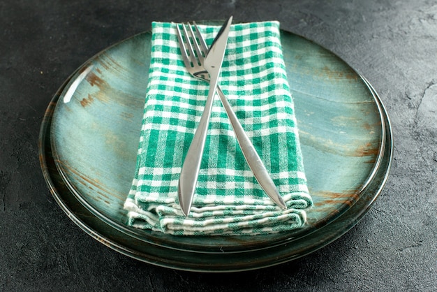 Bezpłatne zdjęcie widok z dołu skrzyżowany nóż obiadowy i widelec na serwetce w zielono-białą kratkę na półmiskach na czarnym stole