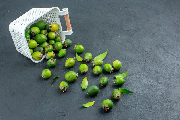 Widok z dołu świeże feijoas rozrzucone z plastikowego kosza na ciemnej powierzchni z miejscem na kopię