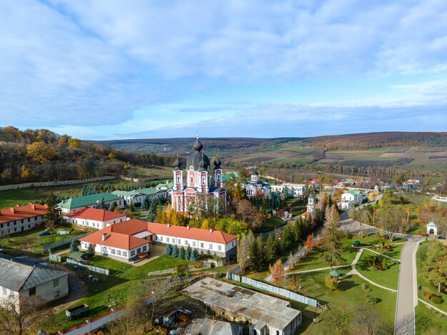 Widok z drona na klasztor Curchi. Kościoły, inne budynki, zielone trawniki i ścieżki spacerowe. Wzgórza z zielenią w oddali. Moldova