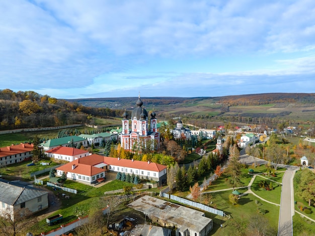 Widok z drona na klasztor Curchi. Kościoły, inne budynki, zielone trawniki i ścieżki spacerowe. Wzgórza z zielenią w oddali. Moldova