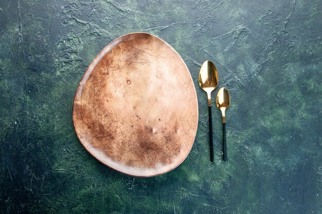 widok z góry brązowy talerz ze złotymi łyżkami na ciemnoniebieskim tle obiad sztućce posiłek jedzenie restauracja naczynie kolor tabeli
