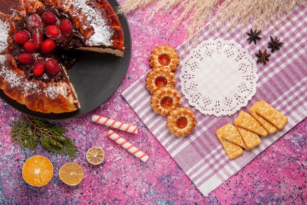 Widok z góry ciasto czekoladowe z truskawkami krakersami i ciasteczkami na różowym biurku słodkie ciasteczka z cukrem