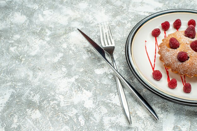Widok z góry ciasto jagodowe na białym owalnym talerzu skrzyżowanym widelcem i nożem obiadowym na szarej powierzchni wolnej przestrzeni
