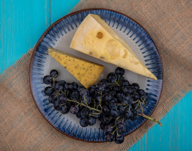 Widok z góry czarne winogrona z plasterkami sera na talerzu na beżowej serwetce