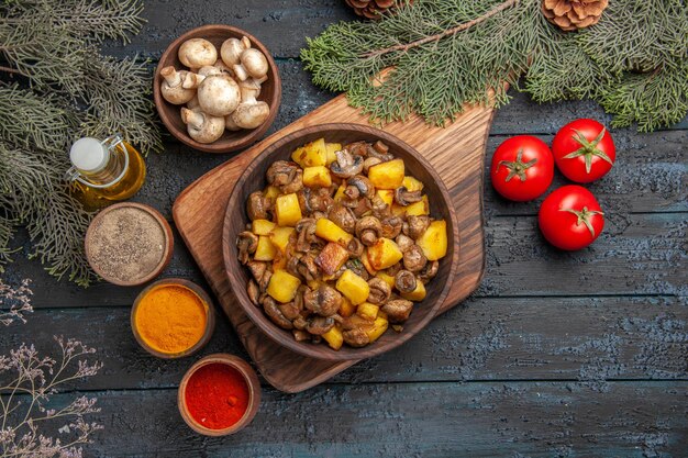 Widok z góry danie i warzywa talerz ziemniaków z grzybami na drewnianej desce obok trzech pomidorów i kolorowych przypraw pod olejem w butelce gałęzie drzew i miska grzybów