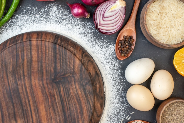 Bezpłatne zdjęcie widok z góry deska posypana mąką ryż w misce jajka czerwona cebula czarny pieprz w drewnianej łyżce na stole
