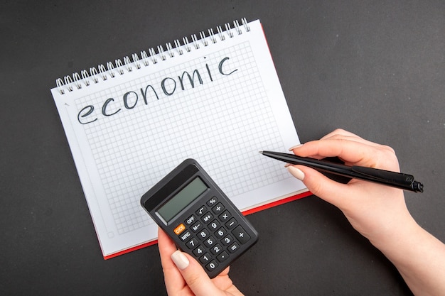 Widok z góry ekonomiczny napisany na spiralnym kalkulatorze notatnika i długopisie w kobiecych rękach na ciemności
