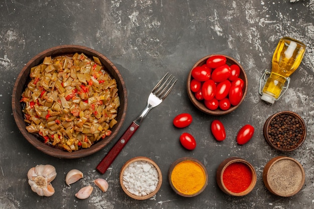 Bezpłatne zdjęcie widok z góry fasolka szparagowa talerz apetycznej fasolki szparagowej z pomidorami obok czosnku widelec do pomidorów butelka oleju miska przypraw na ciemnym stole