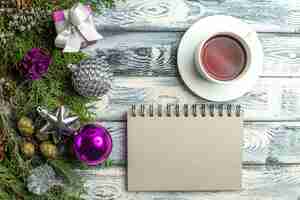 Bezpłatne zdjęcie widok z góry filiżanka herbaty notatnik mały prezent gałęzie jodły świąteczne zabawki na drewnianym tle