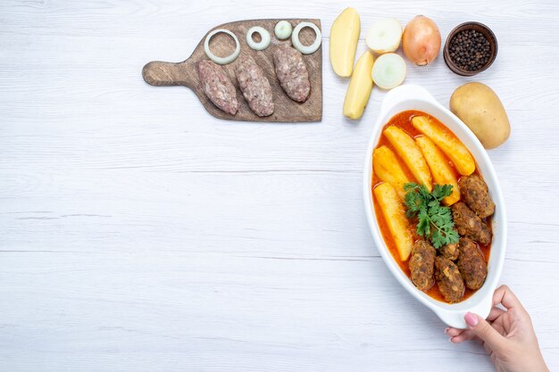Widok z góry gotowanych kotletów mięsnych z sosem ziemniaczanym i zieleniną wraz z surowym mięsem na lekkim biurku, mączka mięsna warzywna