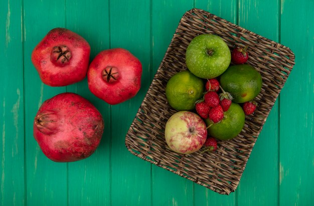 Widok z góry granaty z mandarynkami jabłkami i truskawkami w koszu na zielonej ścianie
