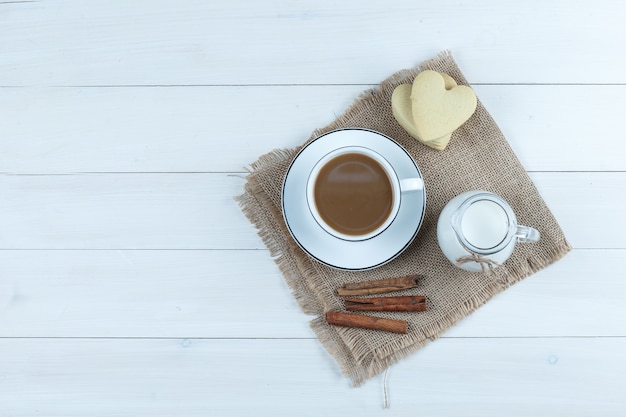Widok z góry kawa w filiżance z ciasteczkami, cynamonem, mlekiem na tle drewnianych i worek.