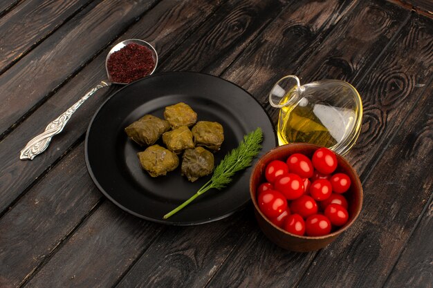 widok z góry mączka z zielonego mięsa dolma wewnątrz czarnego talerza wraz z zieloną oliwą z oliwek i czerwonymi pomidorami cherry na brązowym drewnianym
