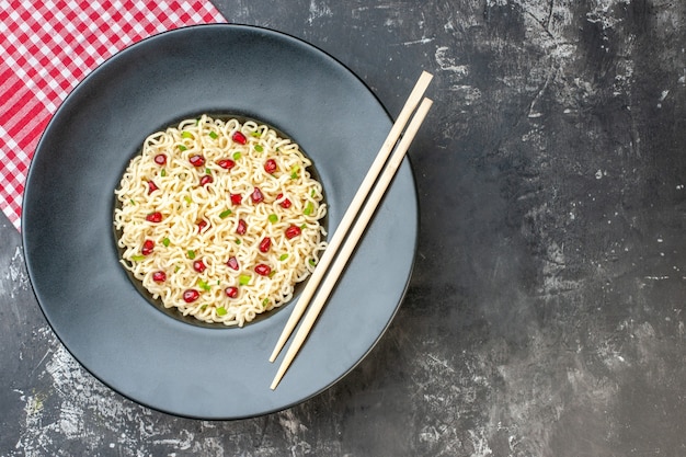 Widok z góry makaron ramen na ciemnym okrągłym talerzu czerwone białe pałeczki w kratkę na ciemnym tle