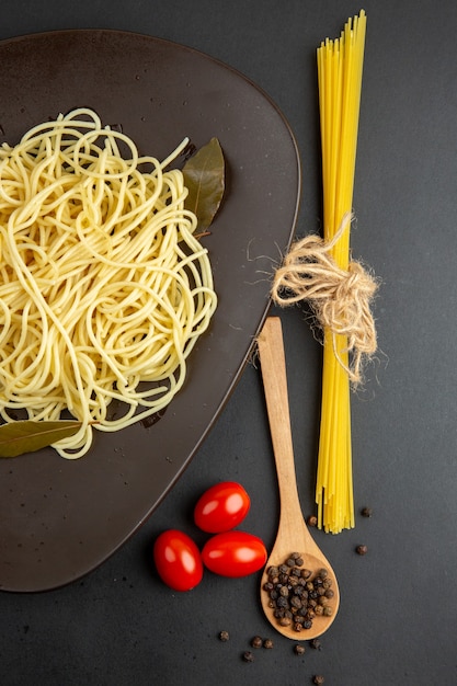 Widok z góry makaron spaghetti z liśćmi laurowymi na talerzu widelec drewniana łyżka pomidorki koktajlowe na czarnej powierzchni