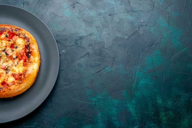 Widok z góry małej okrągłej pizzy z serem uformowanej wewnątrz płyty na ciemnoniebieskiej powierzchni